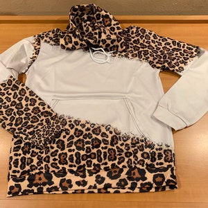 May include: A white hoodie with a leopard print design on the sleeves and hood. The print is a faded, distressed look.