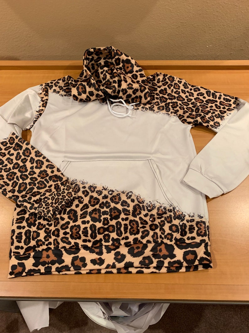 May include: A white hoodie with a leopard print design on the sleeves and hood. The print is a faded, distressed look.