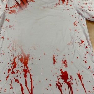 May include: White t-shirt with red splattered paint and claw marks. The shirt has a distressed look.