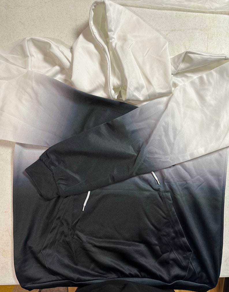May include: A white and black ombre hoodie with a drawstring hood and a kangaroo pocket.
