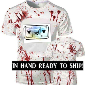 May include: White t-shirt with red blood splatter and a graphic of two playing cards with hearts and the word "and" between them.