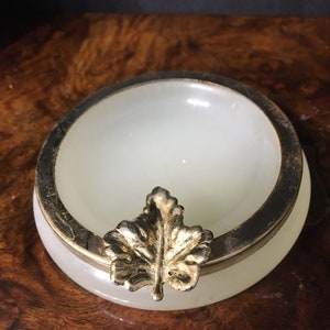 Può includere: Posacenere in alabastro bianco con bordo argentato e un design a foglia d'oro.