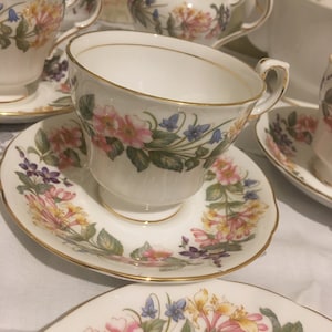 Puede incluir: Un juego de tazas de té y platillos florales vintage. Las tazas y los platillos presentan un delicado patrón floral con flores rosas, amarillas y moradas. Las tazas tienen un borde dorado alrededor del borde.