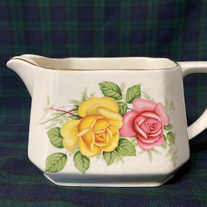 Może przedstawiać: Biały dzbanek do śmietanki z ceramiczną pokrywką z pozłacanym brzegiem i kwiatowym wzorem z różowymi i żółtymi różami.