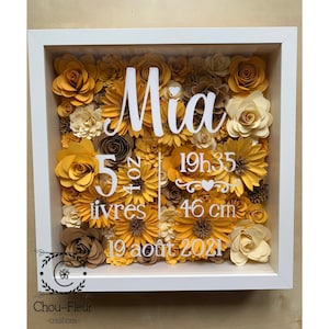 Peut inclure: Une boîte à ombre blanche remplie de fleurs en papier jaunes, brunes et crème. Le nom "Mia" est écrit en lettres blanches, ainsi que les détails de naissance : 5 lb 8 oz, 19 heures 35 minutes, 19 pouces et 19 août 2021.