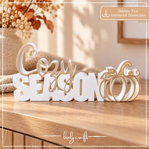 May include: A white and light tan 3D sign featuring the text "Cozy Season" in a layered script and block font, with a pumpkin outline on the right side. The text "Digital File" and "Digitaler Download" appear in the top right corner.