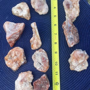 May include: A collection of ten irregular, translucent, and opaque stones in shades of white, tan, and reddish-brown. A yellow Stanley measuring tape is positioned vertically next to the stones, showing a length of approximately 13 inches.
