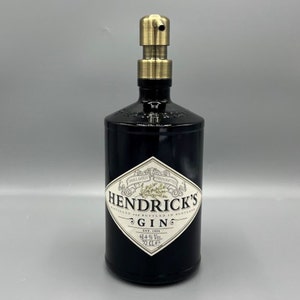 May include: A black glass bottle with a gold pump dispenser. The bottle is labelled "Hendrick's Gin" and has a diamond-shaped label with a botanical illustration.
