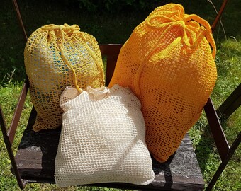 May include: Three crocheted bags, one yellow, one white, and one yellow with a blue lining, are sitting on a wooden swing.