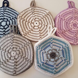 May include: Five crocheted pot holders in different colours, including blue, brown, pink, and white. Each pot holder has a hexagonal shape with a decorative centre.
