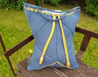 May include: A blue knitted tote bag with yellow crocheted trim and drawstrings. The bag has a wooden toggle on each drawstring.