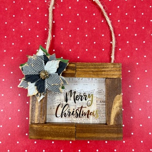 May include: A wooden Christmas ornament with a black and white patterned flower and the words "Merry Christmas" in gold lettering on a sheet of music.