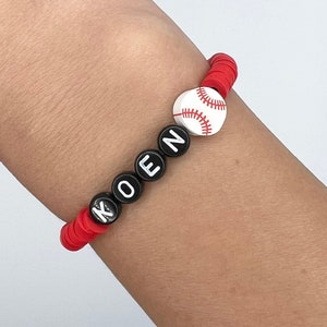 May include: Red and black beaded bracelet with the name "KOEN" spelled out in black beads and a white baseball charm.