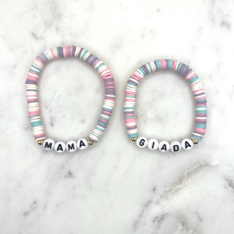 May include: Two colourful beaded bracelets with the names "MAMA" and "GIADA" spelled out in black letters on white beads.