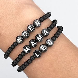 May include: Three black beaded bracelets with white lettering spelling out the names "KOEN", "MAMA", and "LEO".