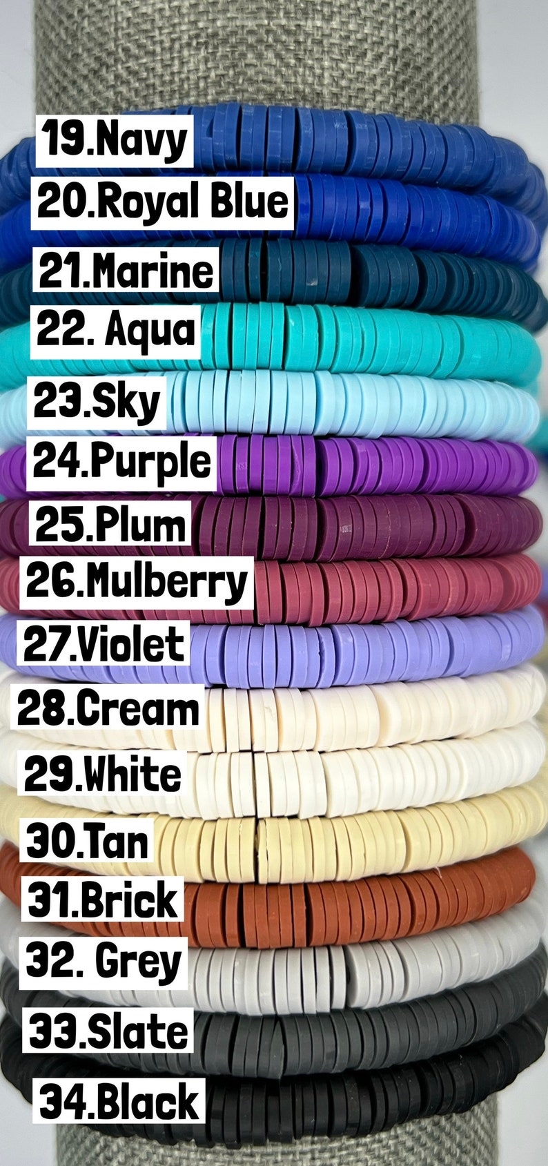 May include: A close-up of 16 different colours of round polymer clay beads. The beads are stacked on top of each other, with the colours labelled from 19 to 34. The colours include navy, royal blue, marine, aqua, sky, purple, plum, mulberry, violet, cream, white, tan, brick, grey, slate, and black.