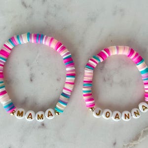 May include: Two colourful beaded bracelets with white letter beads spelling out the names "MAMA" and "JOANNA".