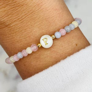 May include: A bracelet with pastel-colored beads and a gold charm with the letter "P" on a white background.