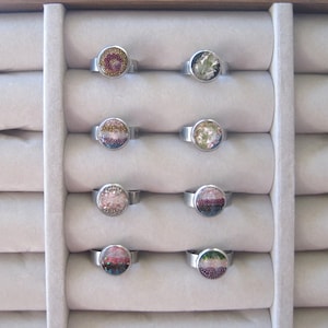 May include: Eight silver rings with different colored glass insets. The rings are displayed in a white ring holder.