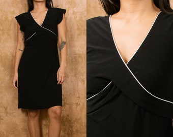 May include: A black dress with a V-neckline and white trim. The dress has short sleeves with a ruffled detail and a wrap-style bodice. The dress is knee-length and appears to be made of a soft, flowing fabric.
