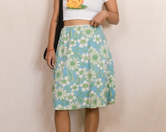 May include: A white crop top with a cartoon bunny and the text "Sorry the bunny". A blue skirt with white and green floral pattern. The outfit is completed with black sandals and a black shoulder bag.