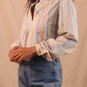 Peut inclure: Un chemisier &agrave; rayures pastel avec un col officier et des manches longues. Le chemisier pr&eacute;sente des rayures verticales dans les tons rose, bleu et jaune. Les manches ont des poignets boutonn&eacute;s. Le chemisier est associ&eacute; &agrave; un jean en denim bleu.