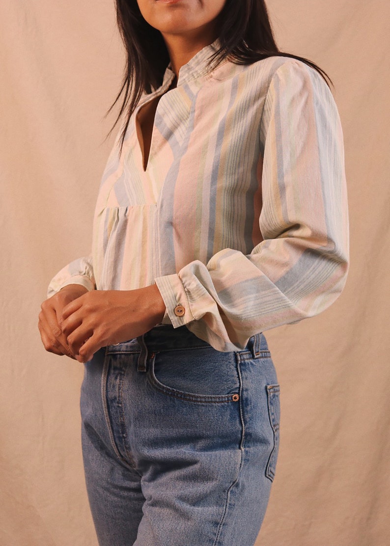 Peut inclure: Un chemisier &agrave; rayures pastel avec un col officier et des manches longues. Le chemisier pr&eacute;sente des rayures verticales dans les tons rose, bleu et jaune. Les manches ont des poignets boutonn&eacute;s. Le chemisier est associ&eacute; &agrave; un jean en denim bleu.