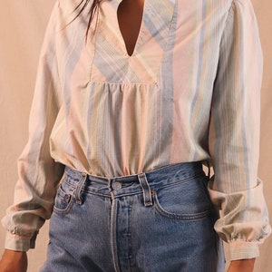 Peut inclure: Un chemisier &agrave; rayures pastel avec un col officier et un d&eacute;collet&eacute; en V. Le haut &agrave; manches longues est associ&eacute; &agrave; un jean en denim bleu. Le chemisier pr&eacute;sente des rayures verticales roses, bleues, jaunes et blanches.