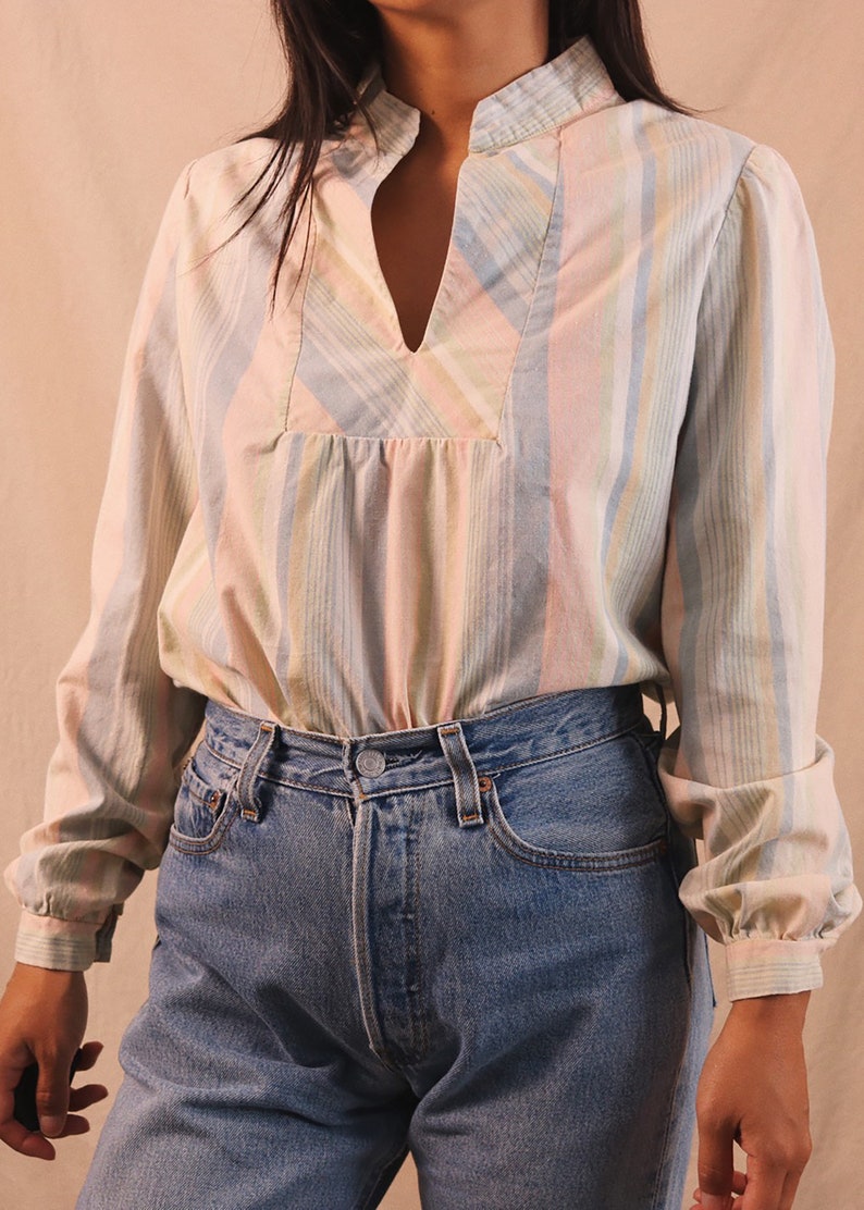 Peut inclure: Un chemisier &agrave; rayures pastel avec un col officier et un d&eacute;collet&eacute; en V. Le haut &agrave; manches longues est associ&eacute; &agrave; un jean en denim bleu. Le chemisier pr&eacute;sente des rayures verticales roses, bleues, jaunes et blanches.