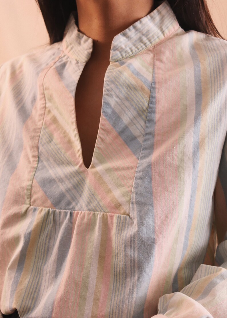 Peut inclure: Chemise &agrave; rayures pastel avec col officier et encolure en V. La chemise pr&eacute;sente des rayures verticales roses, bleues, jaunes et blanches. Le tissu semble &ecirc;tre un m&eacute;lange l&eacute;ger de coton ou de lin.