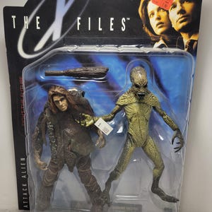 May include: The X-Files action figure set features two figures: a green alien and a brown humanoid figure. The figures are packaged in a clear plastic blister pack with a blue and white background. The packaging features the X-Files logo and the text "Fight the Future".