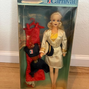 May include: A Captain Carnival doll in its original packaging. The doll is wearing a white uniform with gold accents and a navy hat. The packaging includes a red dress and navy outfit. The box has the Carnival logo and the text "Recommended For Ages 3 and Up."