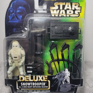 May include: A Star Wars Deluxe Snowtrooper action figure in its original packaging. The figure is white and tan, with a black repeating blaster and a swivel turret. The packaging features Darth Vader and the Star Wars logo.