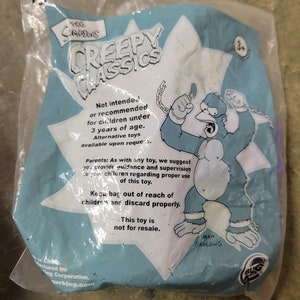 May include: A blue plastic bag with a cartoon image of a gorilla wearing a chain. The bag has the text "The Simpsons Creepy Classics" and "Not intended or recommended for children under 3 years of age." The bag also has the text "Keep bag out of reach of children and discard properly. This toy is not for resale."