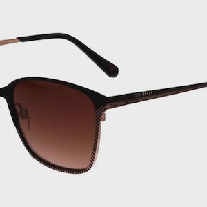May include: Ted Baker sunglasses featuring a black and rose gold frame with a textured, striped pattern along the outer edges. The lenses are a gradient brown tint, and the temples are thin with black tips. The brand name is printed on the temple.
