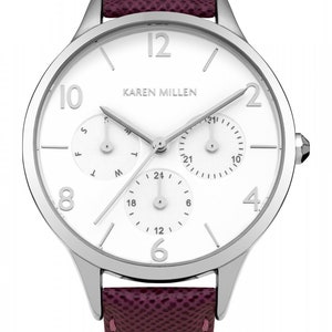 May include: A silver-toned watch with a white face and three subdials. The watch has a burgundy leather band with white stitching.