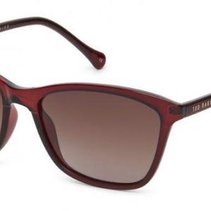 May include: Translucent deep red sunglasses with a rounded rectangular frame and gradient brown lenses. The inner temple features the text TED BAKER and the phrase A RAY OF SUNSHINE, while the outer temple displays the brand name TED BAKER.