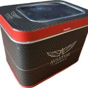 May include: A rectangular watch box with a carbon fibre pattern and red trim. The box has a clear top and the word "AVIATOR" with a wing logo is printed on the side.