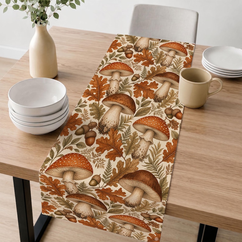 May include: A rectangular table runner featuring a repeating pattern of brown and orange mushrooms, acorns, and oak leaves on a cream background. The design includes various mushroom shapes with detailed caps and stems, interspersed with foliage.