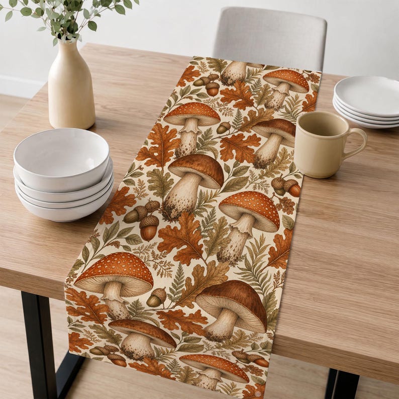 May include: A rectangular table runner featuring a repeating pattern of brown and orange mushrooms, acorns, and oak leaves on a cream background. The design includes various mushroom shapes with detailed caps and stems, interspersed with foliage.