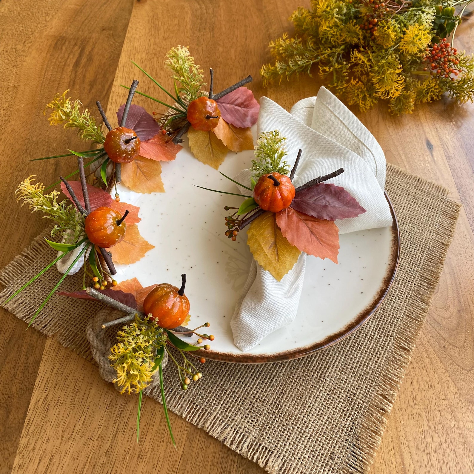 A Harvest Ring with Tiny Pumpkins and Leaves Pale cloth napkins gathered through decorative rings with small pumpkins, leaves and autumn accents.