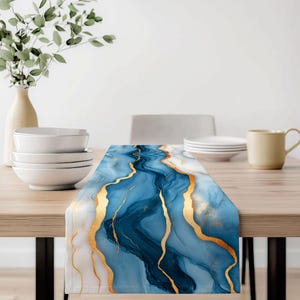 May include: A blue and gold table runner with a marble design. The runner features a flowing pattern of blue and white with gold accents. The runner is rectangular and placed on a wooden table.