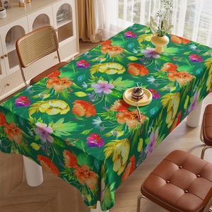 May include: A rectangular tablecloth with a vibrant floral pattern. The design features large, colourful flowers in shades of orange, yellow, and purple against a deep green background. The tablecloth is spread over a table, with a small plate of cake on top.