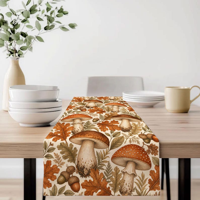 May include: A rectangular table runner featuring a repeating pattern of various mushrooms, brown oak leaves, and acorns in shades of orange, brown, and cream. The design includes detailed illustrations of fungi with spotted caps and stems.