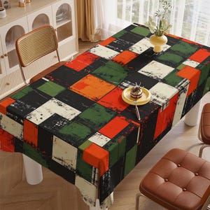 May include: A rectangular tablecloth with a geometric pattern of squares in black, red, green, orange, and cream. The tablecloth is on a wooden table with a yellow vase and a small plate with a dessert on top.
