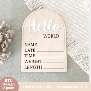 Op de afbeelding: Een houten bord met een afgeronde bovenkant en de tekst "Hello World" in witte letters. Het bord heeft lege regels om de naam, datum, tijd, gewicht en lengte van een pasgeboren baby in te vullen.