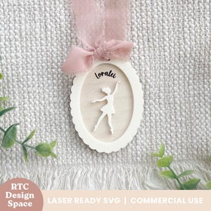 以下が含まれることがあります： 楕円形のフレームの中にバレリーナのシルエットが入った白い木製オーナメント。 バレリーナの上には「Loralai」という名前が書かれています。 ピンクのリボンが上部に付いています。 オーナメントは、テクスチャード加工された背景に吊り下げられています。