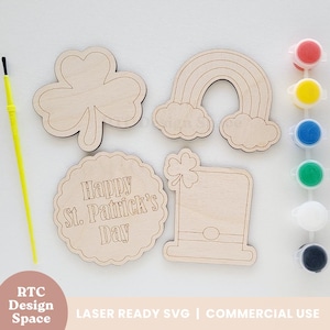 May include: A set of five unfinished wooden shapes for painting, featuring a shamrock, rainbow, leprechaun hat, and two signs that say "Happy St. Patrick's Day". The shapes are ready for painting with the included set of six paint pots.