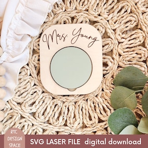 May include: A wooden cutout with a circle in the center and the text "Mrs. Young" at the top. The cutout is on a woven surface.