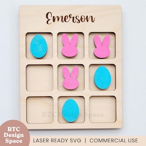 May include: Wooden tic-tac-toe board with laser-cut Easter-themed pieces. The board features the name "Emerson" at the top. The game pieces include pink bunnies and turquoise eggs. The bottom right corner has the text "RTC Design Space".